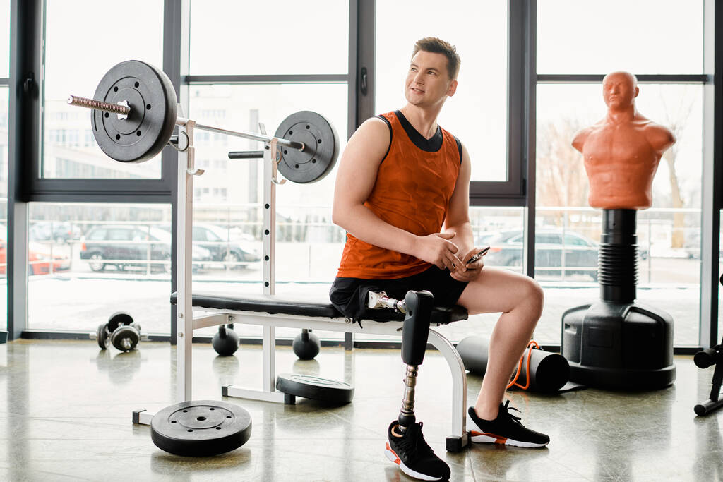 Egy mozgássérült férfi műlábakkal ül egy padon egy edzőteremben, szüneteltetve az edzéstervét.. - Fotó, kép