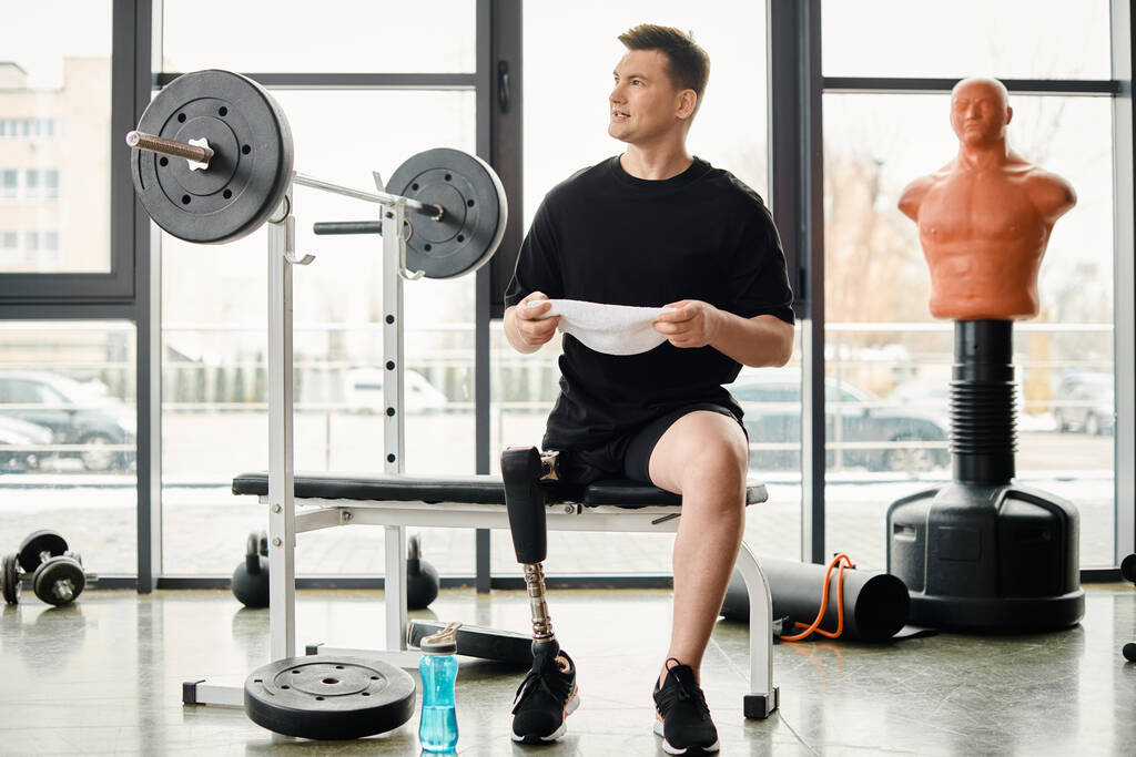 Człowiek z protezą nogi siedzi na ławce gimnastycznej, głęboko w myślach, gdy robi sobie przerwę od rutyny treningowej.. - Zdjęcie, obraz
