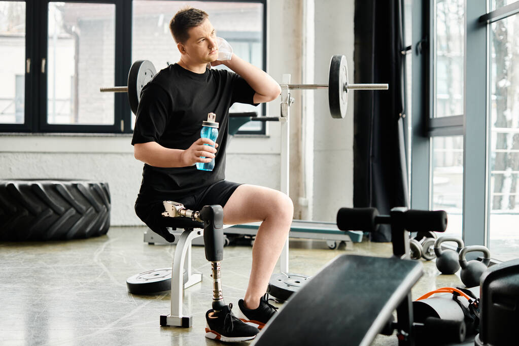 Ein Mann mit Beinprothese sitzt auf einer Bank und hält eine Flasche Wasser in der Hand. - Foto, Bild