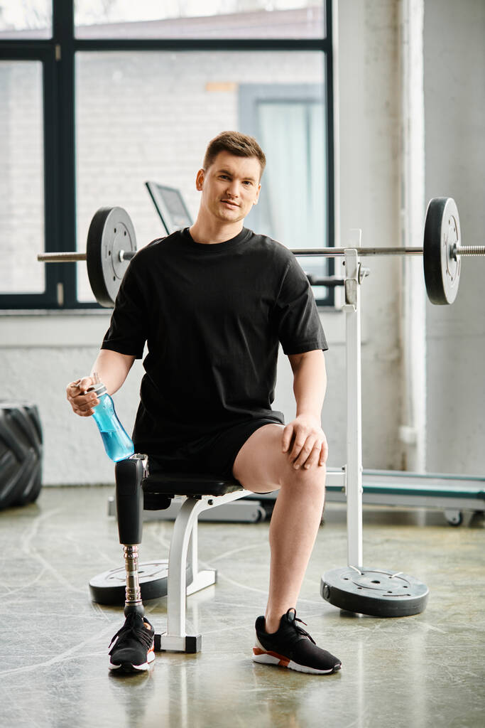 Un hombre decidido con una pierna protésica se sienta en una silla, cerca de una barra en un gimnasio, mostrando fuerza y resistencia. - Foto, Imagen