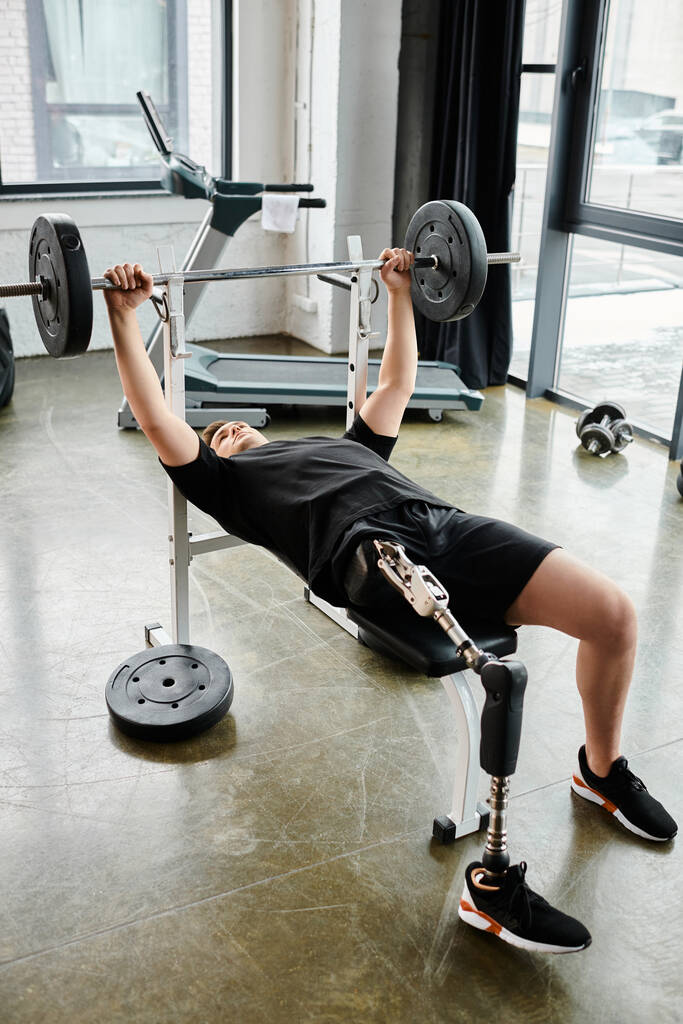 Un homme, avec une prothèse de jambe, effectue un exercice de presse banc avec un haltère à la salle de gym. - Photo, image