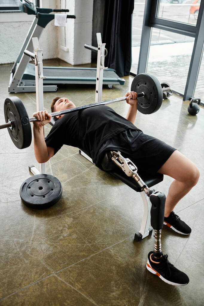 Człowiek z protezą nogi wykonuje wyciskanie na ławce ze sztangą w siłowni.. - Zdjęcie, obraz