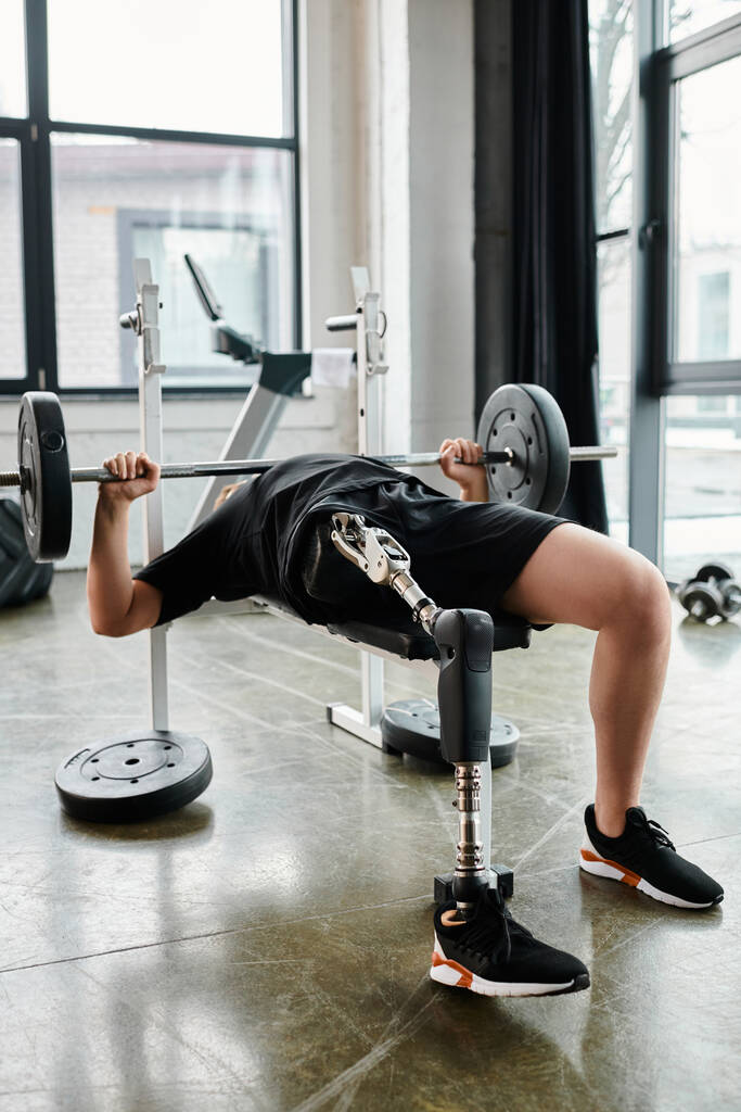 Un homme, avec une prothèse de jambe, soulevant un haltère tout en faisant une presse banc dans une salle de gym. - Photo, image