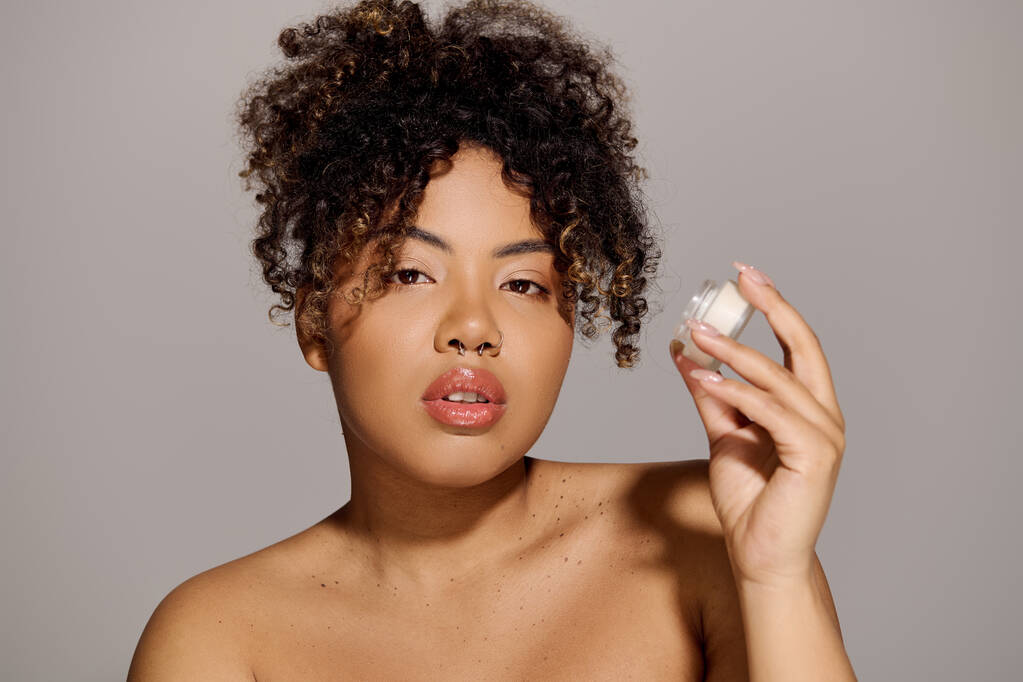 Jeune femme afro-américaine aux cheveux bouclés tenant un pot de crème visage - Photo, image