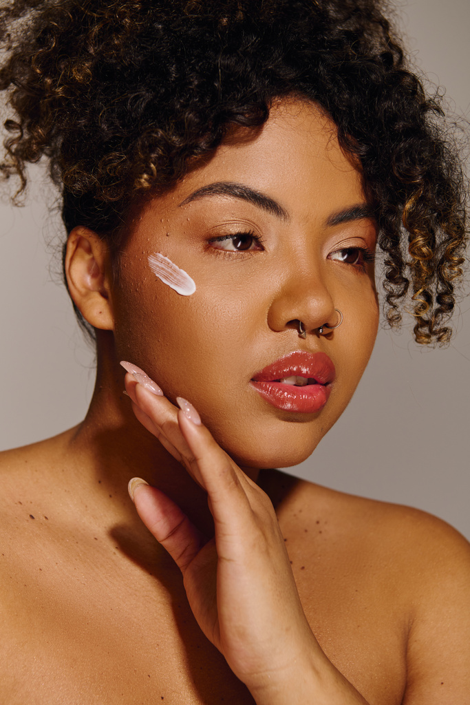 A beautiful young African American woman with curly hair showcasing a white cream on her cheek in a studio setting. - Photo, Image