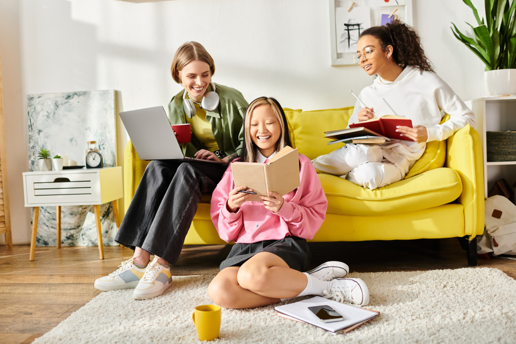 Μια ποικιλόμορφη ομάδα εφήβων κοριτσιών κάθονται στενά μαζί σε ένα ζωντανό κίτρινο καναπέ, απορροφημένοι στη μελέτη και βαθιά στη συζήτηση. - Φωτογραφία, εικόνα