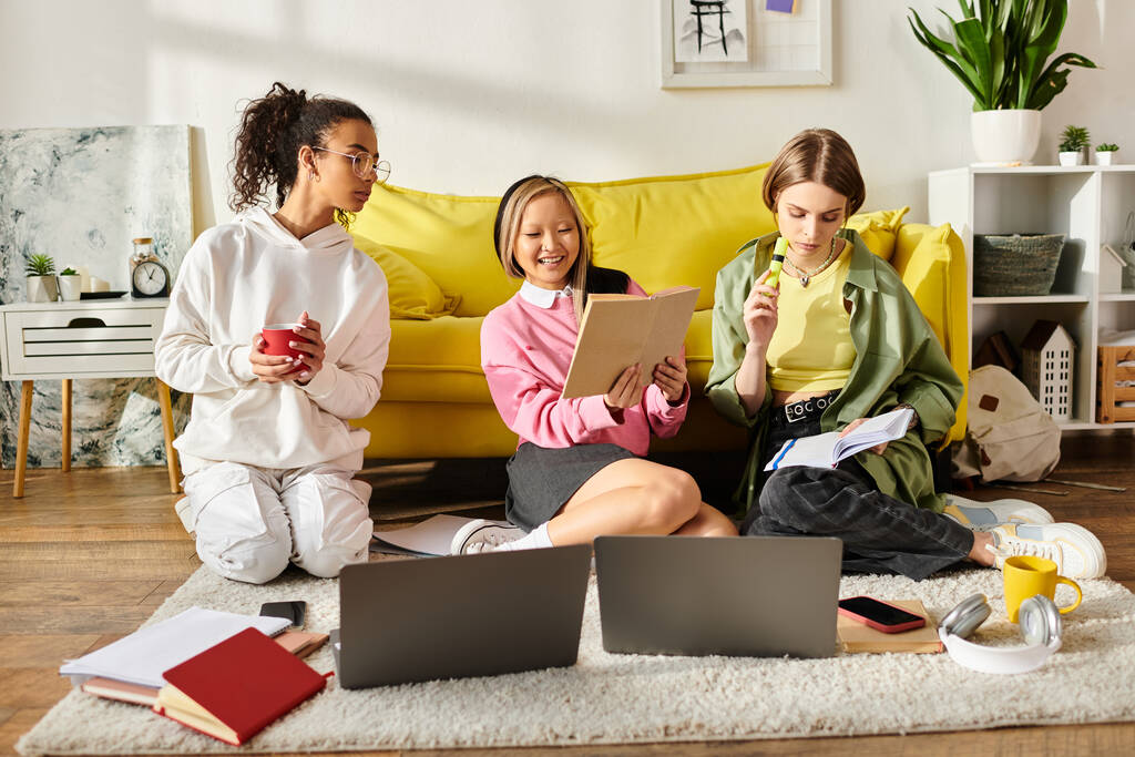 Drei Teenager verschiedener Rassen sitzen auf dem Boden, vertieft in ihre Laptops, und lernen zusammen. - Foto, Bild