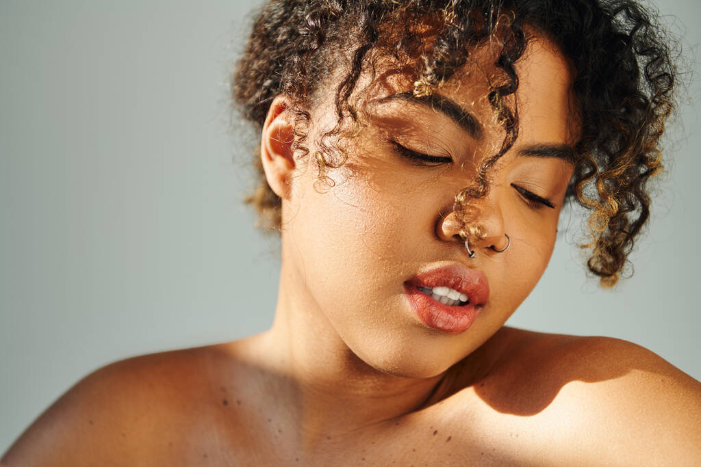 Un primer plano de una hermosa mujer afroamericana con un anillo en la nariz posando sobre un vibrante telón de fondo. - Foto, imagen