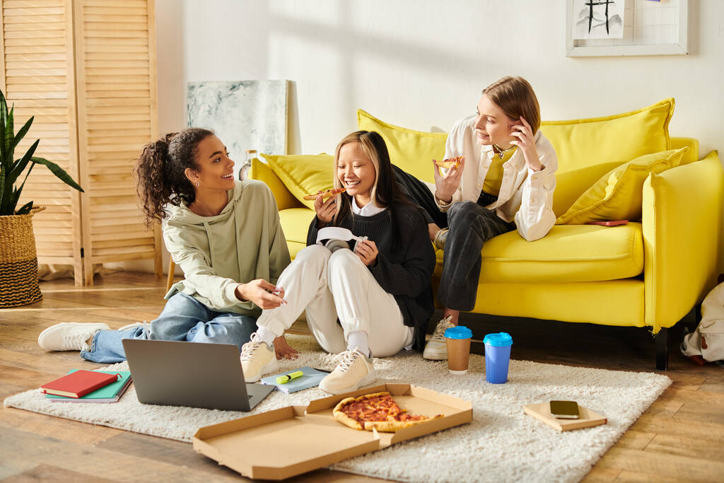 Grupa różnorodnych nastolatek rozmawia i śmieje się siedząc na podłodze obok żywej, żółtej kanapy w przytulnym otoczeniu domowym. - Zdjęcie, obraz