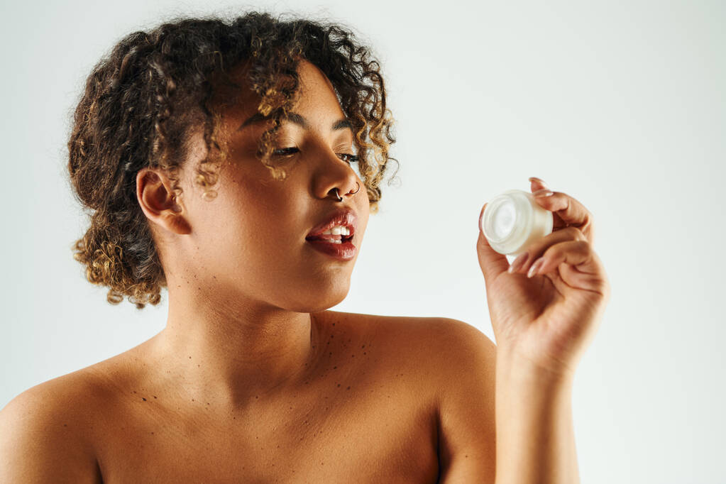 アフリカ系アメリカ人女性は活気に満ちた背景に対してクリームボトルを保持. - 写真・画像