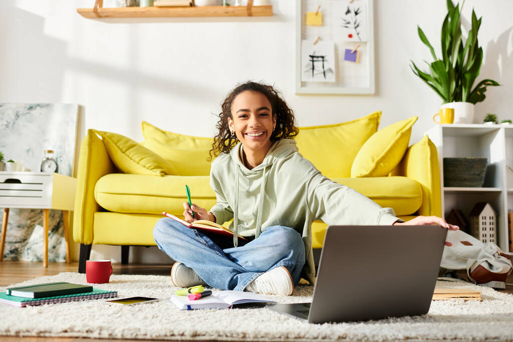 Een tienermeisje zit op de vloer, gefocust op haar laptop scherm, actief bezig met e-learning thuis. - Foto, afbeelding