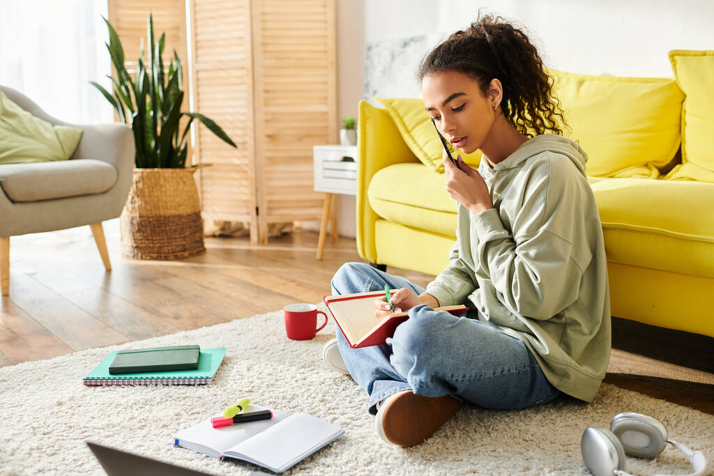 Een tienermeisje dat op de vloer zit, met een mobiele telefoon voor e-learning, volledig betrokken bij virtuele studiesessies. - Foto, afbeelding