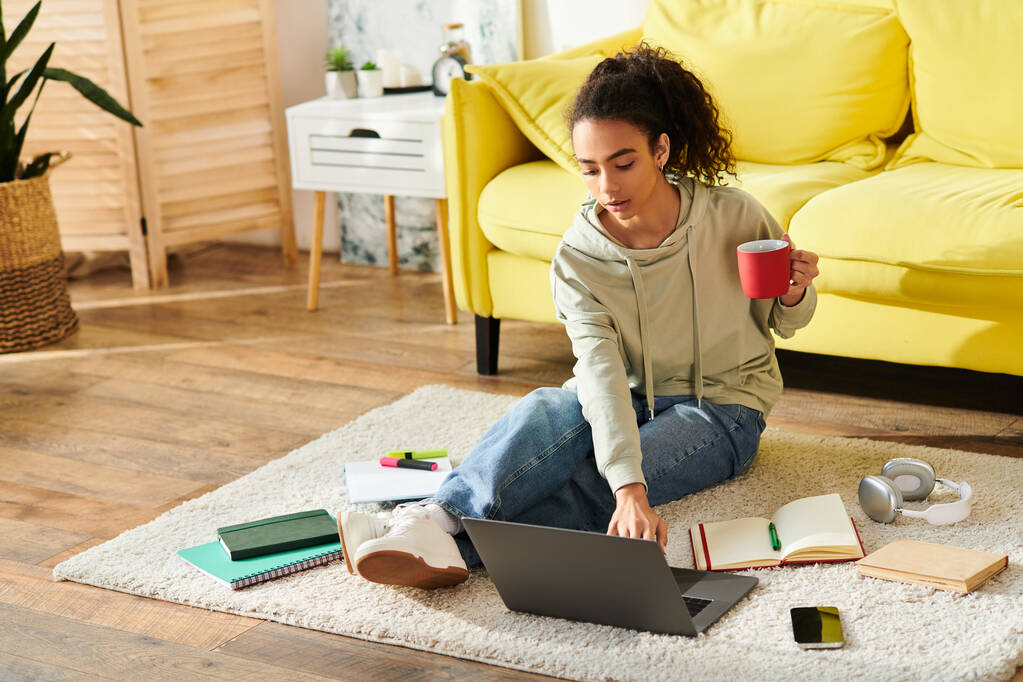 Un'adolescente seduta sul pavimento, assorta nell'e-learning sul suo portatile, accompagnata da una tazza di caffè. - Foto, immagini
