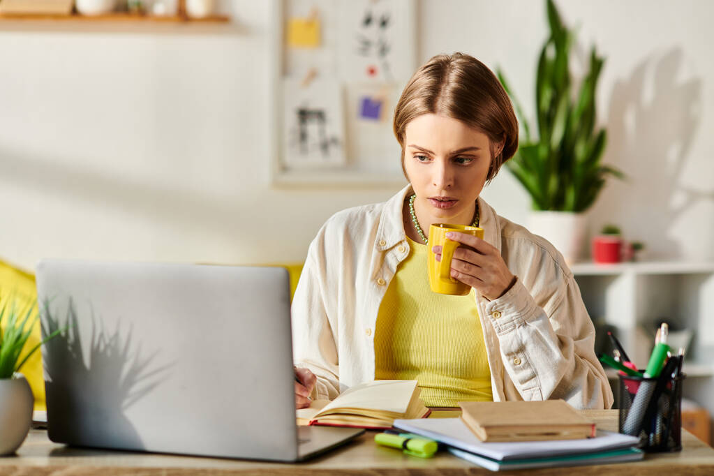 Una adolescente se sienta en un escritorio con una computadora portátil y una taza de café, centrada en su sesión de aprendizaje electrónico. - Foto, imagen