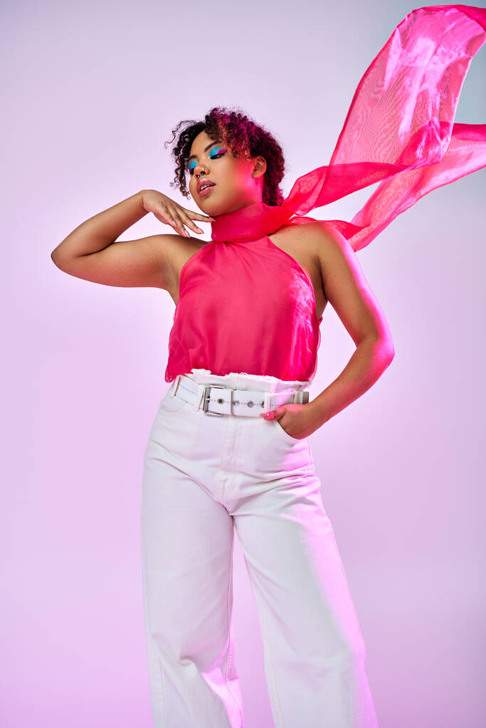 Una hermosa mujer afroamericana posa activamente en un top rosa y pantalones blancos sobre un vibrante telón de fondo. - Foto, Imagen