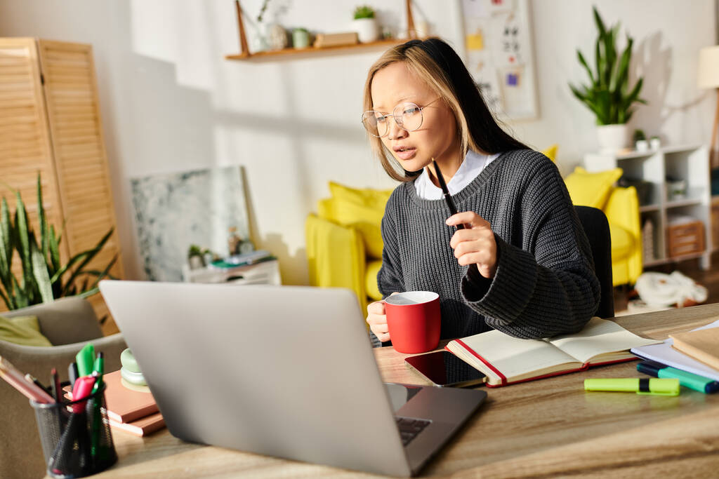 Eine fokussierte junge Asiatin in ihrem Laptop, die zu Hause mit E-Learning beschäftigt ist. - Foto, Bild