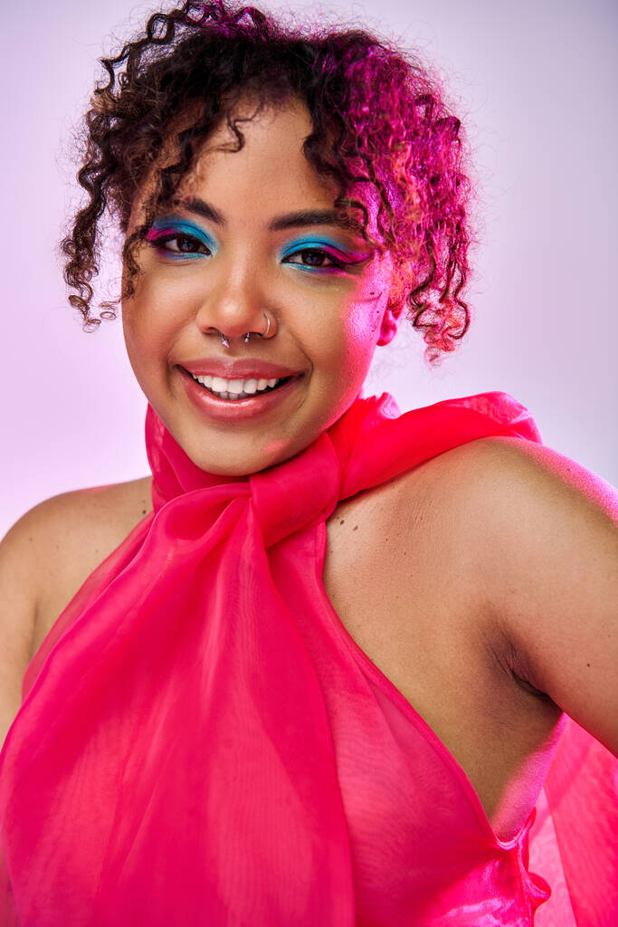 Afro-Amerikaanse vrouw in een roze jurk glimlacht blij voor de camera. - Foto, afbeelding