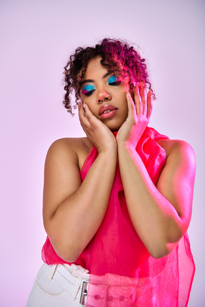 donna afroamericana in un top rosa, tenendo il viso con le mani in contemplazione. - Foto, immagini