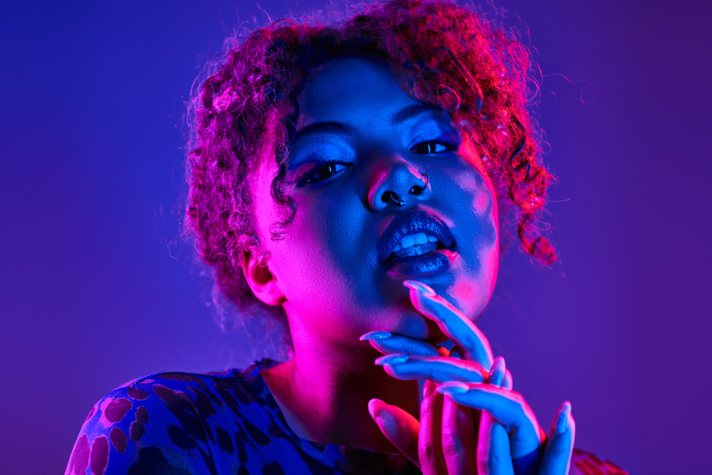 Een opvallende Afro-Amerikaanse vrouw poseert met levendige krullend haar en gedurfde blauwe make-up. - Foto, afbeelding