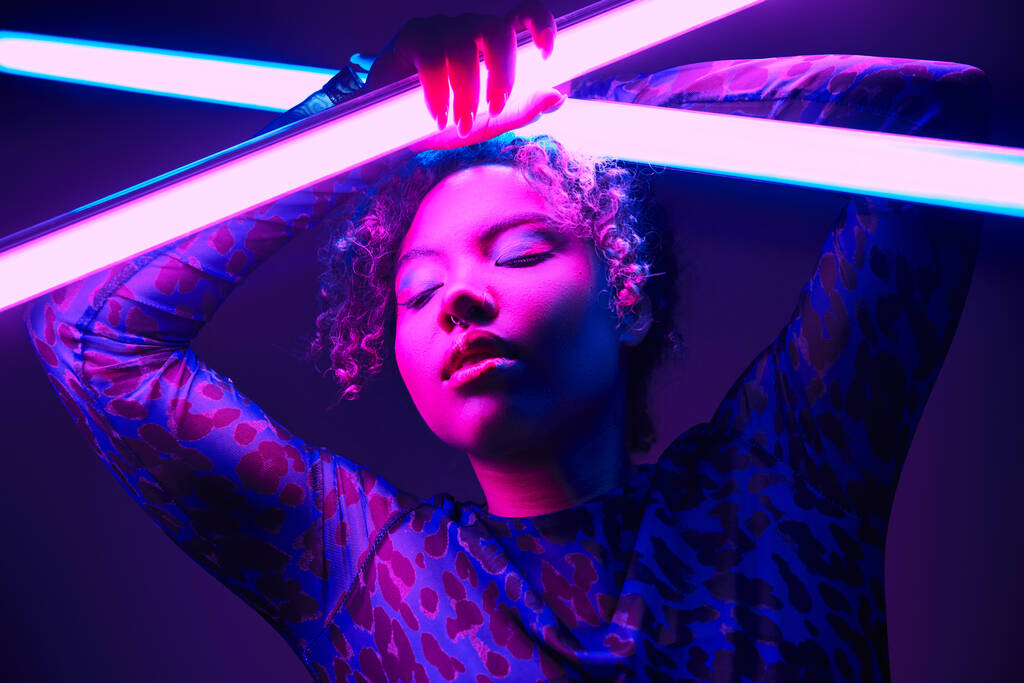 Eine aktive Afroamerikanerin hält selbstbewusst eine leuchtende LED-Lampe in der Hand. - Foto, Bild