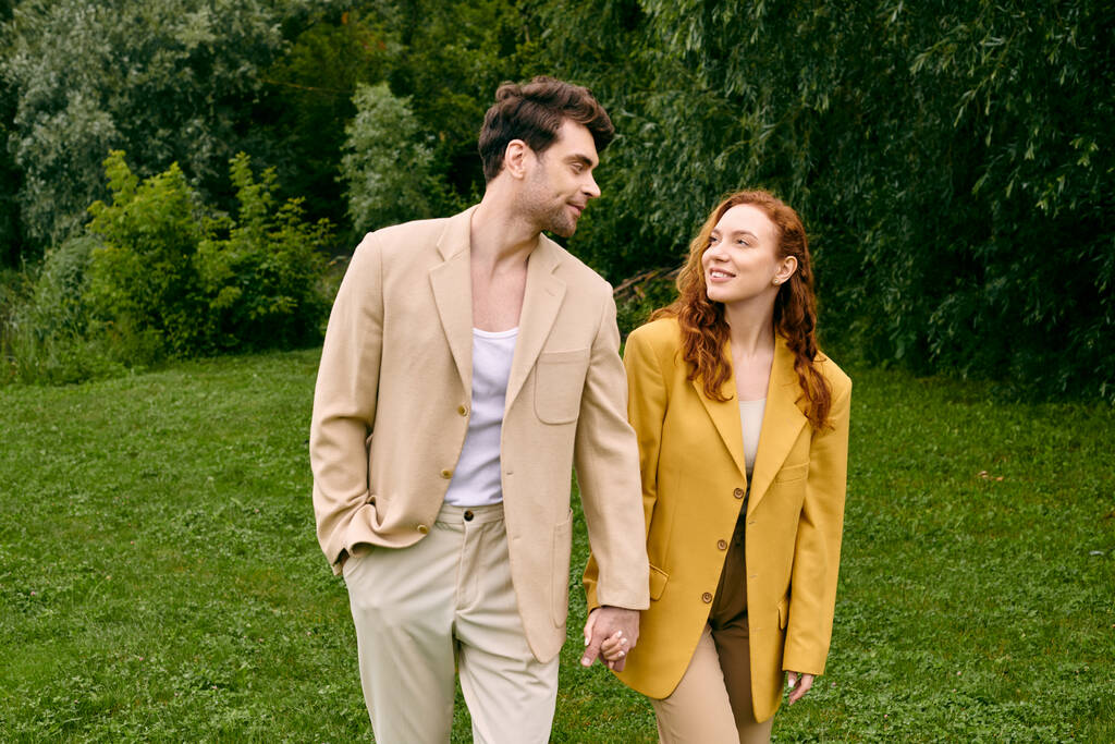 Egy pár, akik egy romantikus randit élveznek, kéz a kézben sétálnak egy buja zöld mezőn, körülvéve természeti szépséggel.. - Fotó, kép