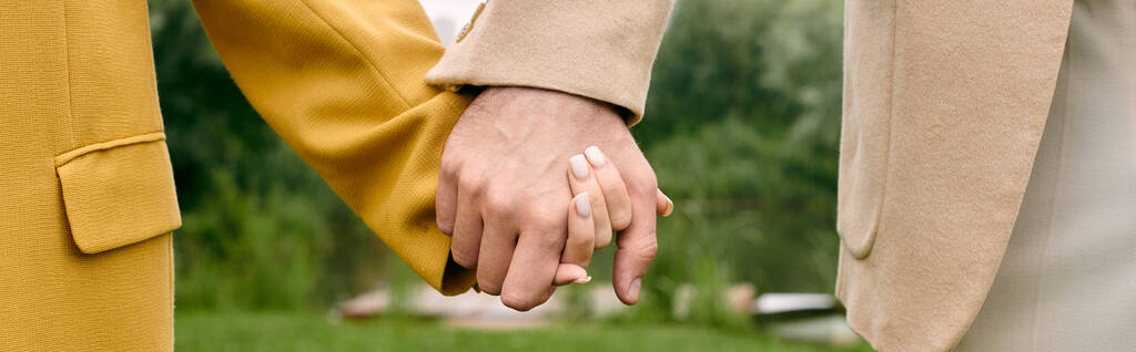 Een close-up van twee mensen die elkaars hand vasthouden, hun vingers verstrengeld in een prachtige groene parksetting. - Foto, afbeelding