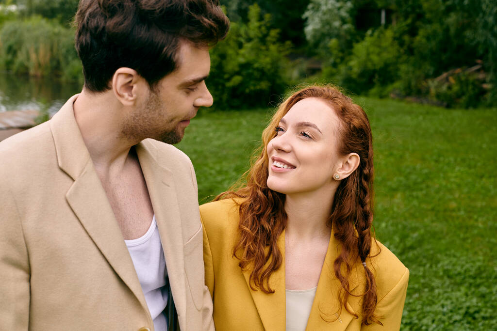 Mężczyzna i kobieta stoją obok siebie w bujnym, zielonym parku, ciesząc się romantyczną randką. - Zdjęcie, obraz