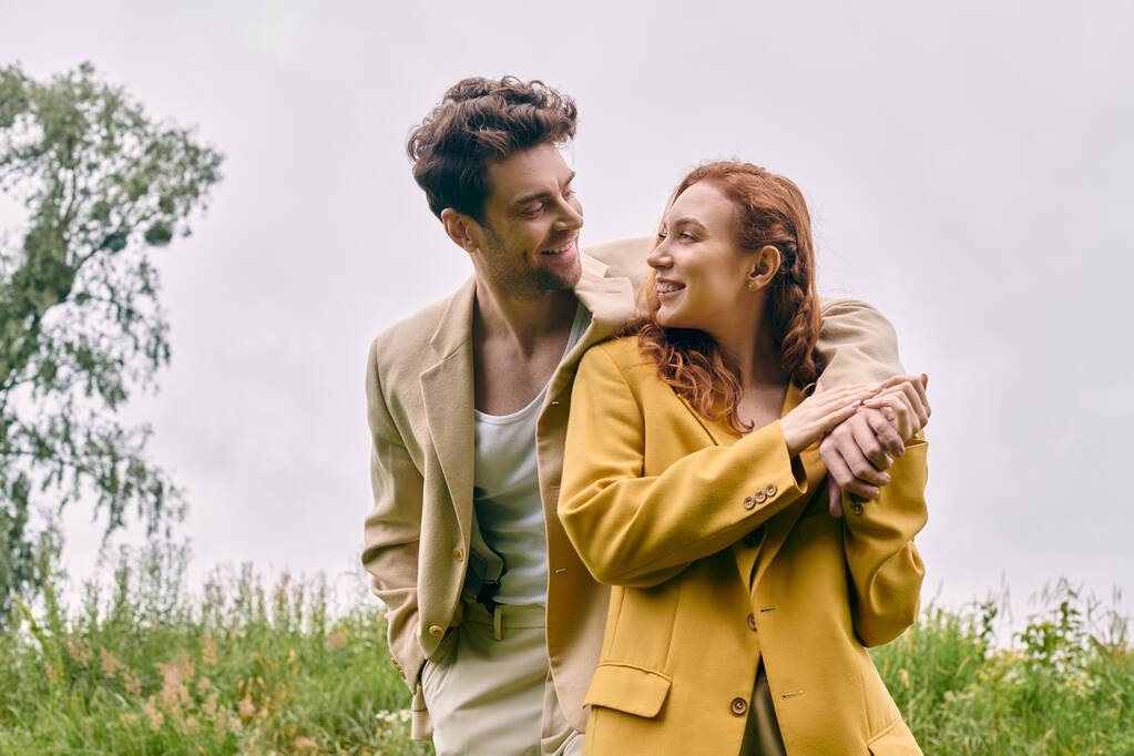 Mężczyzna i kobieta stoją razem na bujnym polu, ciesząc się spokojną romantyczną randką w sercu natury piękna. - Zdjęcie, obraz