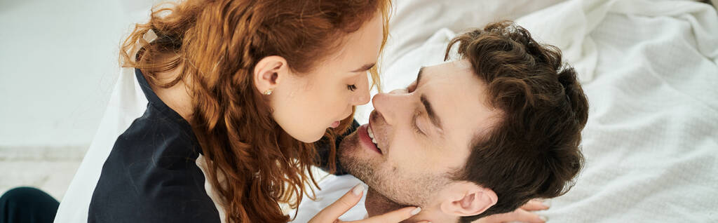 A man tenderly kisses a woman on the cheek, expressing love and affection in a cozy bedroom setting. - Photo, Image