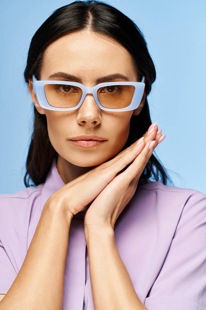 Egy divatos nő lila ingben és elegáns szemüvegben pózol egy stúdióban, nyári hangulattal a kék háttérben.. - Fotó, kép