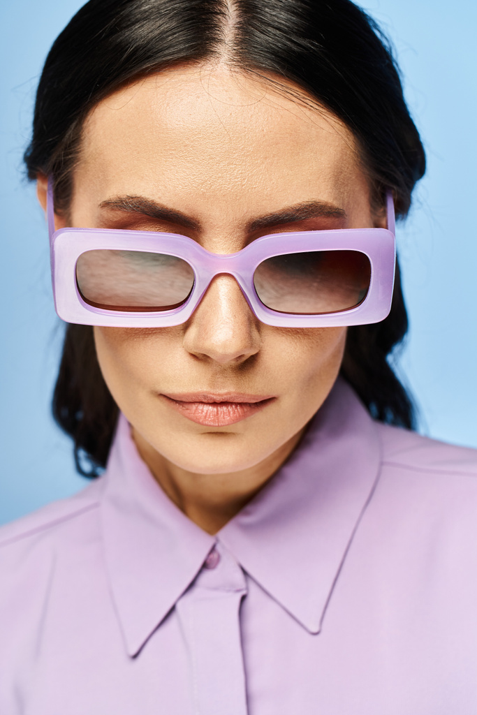 Una mujer de moda emana vibraciones veraniegas en una camisa púrpura y gafas de sol a juego contra un fondo de estudio azul. - Foto, Imagen