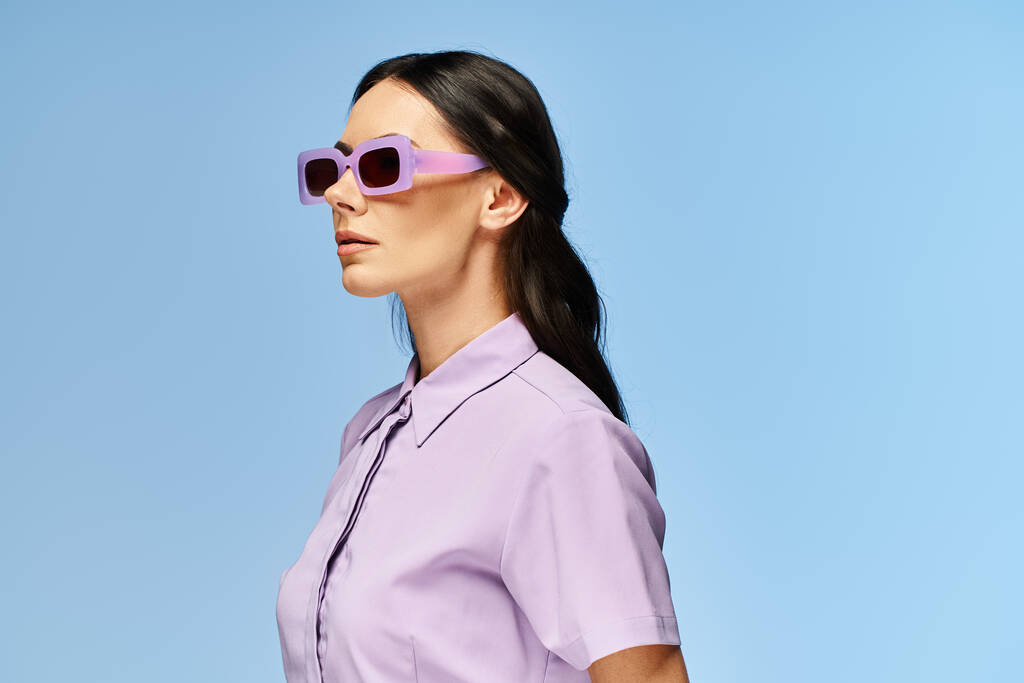 Tyylikäs nainen aurinkolasit ja violetti paita aiheuttaa luottavaisesti vastaan elinvoimainen sininen studio tausta. - Valokuva, kuva