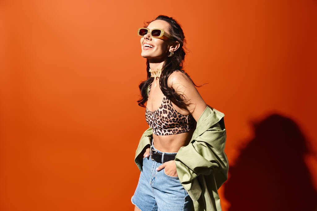 Eine modische Frau, die ein Oberteil mit Leopardenmuster und Jeanshosen trägt und auf orangefarbenem Hintergrund Selbstbewusstsein und Stil ausstrahlt. - Foto, Bild