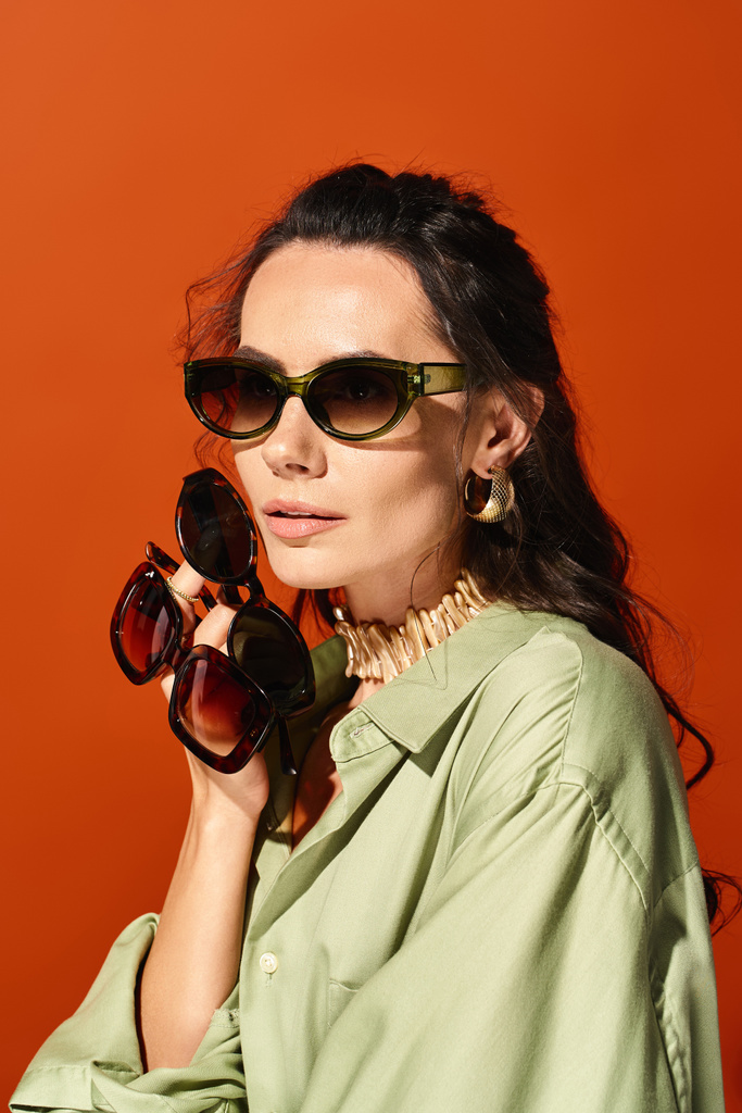 Стильна жінка викриває літній час у зеленій сорочці та модних сонцезахисних окулярах на помаранчевому фоні. - Фото, зображення
