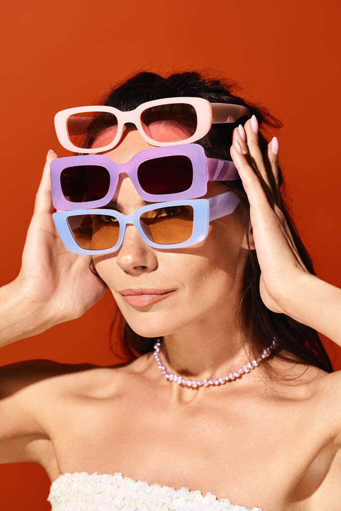 Приголомшлива жінка в білій сукні і фіолетових сонцезахисних окулярах позує в студії на помаранчевому фоні, втілюючи літню моду. - Фото, зображення