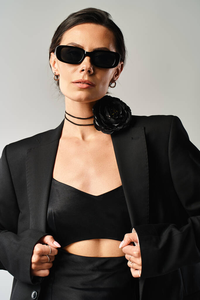 Stylová žena vyzařuje důvěru v černý oblek a sluneční brýle v profesionální focení na šedém pozadí. - Fotografie, Obrázek