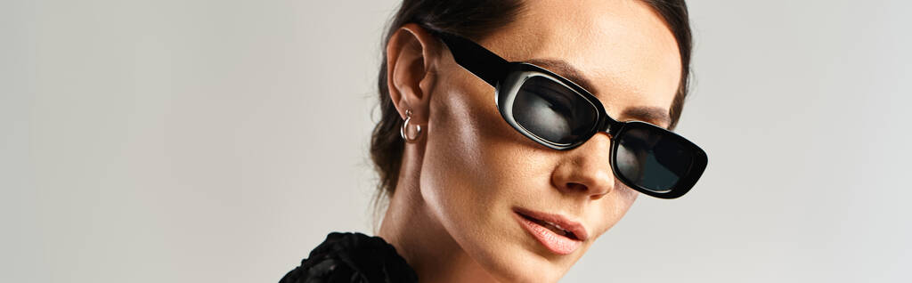 Модна жінка виявляє впевненість у чорній сукні та сонцезахисних окулярах, позуючи на сірому фоні в студії. - Фото, зображення