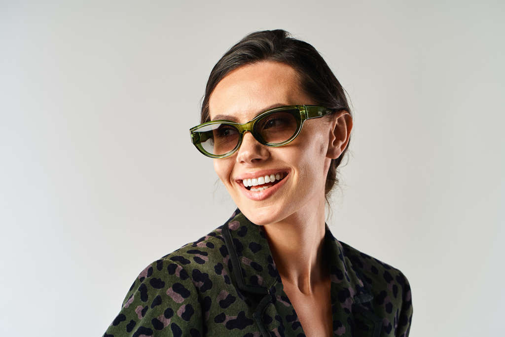 Eine stilvolle Frau mit Sonnenbrille strahlt in einem Atelier vor grauem Hintergrund Glück aus. - Foto, Bild