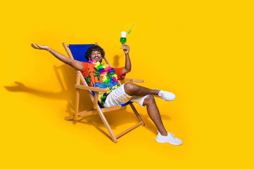Kuva mukava mies käyttää tulosta Havaiji paita nauttia juoma kämmen näyttää tyhjää tilaa rentouttava kansituoli eristetty keltainen väri tausta. - Valokuva, kuva