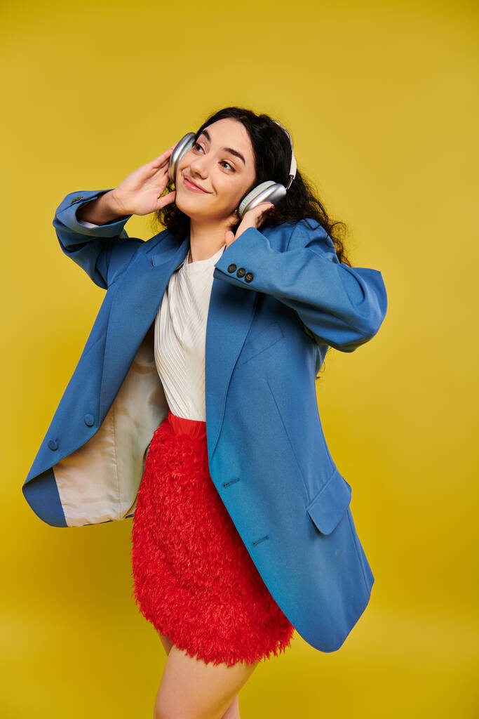Una giovane donna bruna dai capelli ricci trasuda stile e fiducia in una giacca blu e una gonna rossa su uno sfondo giallo vibrante. - Foto, immagini