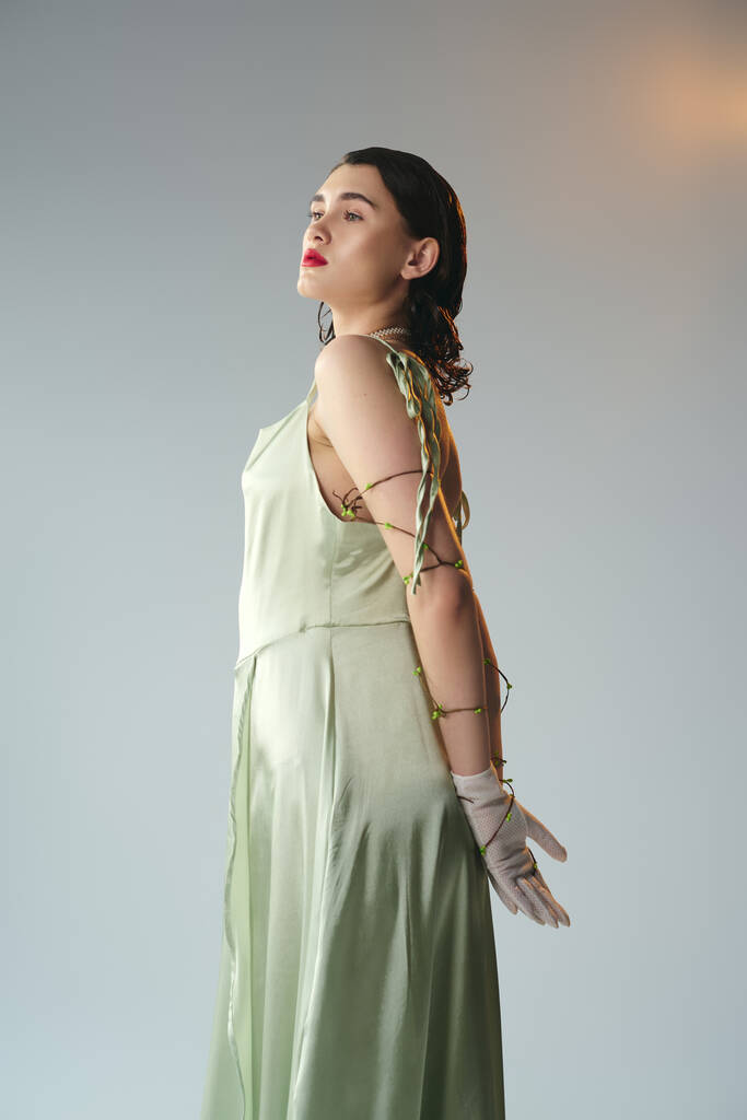A young woman with red lips striking a pose in a green dress and gloves in a studio setting on a grey background. - Photo, Image