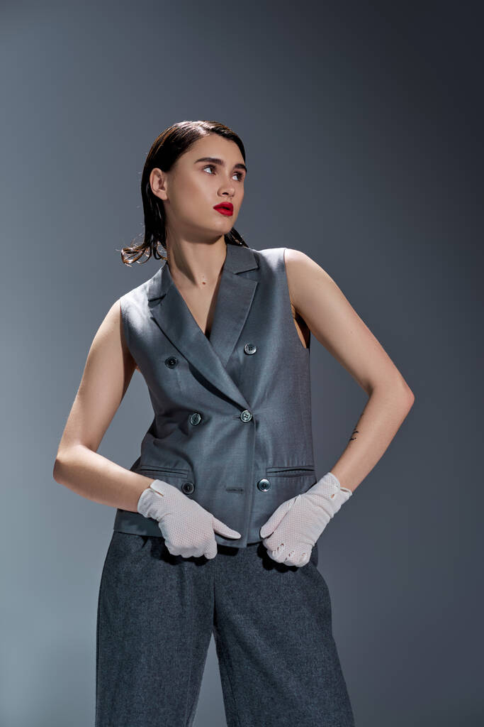 A stylish young woman strikes a pose in a gray suit with a vest, complemented by white gloves, set against a grey background. - Photo, Image