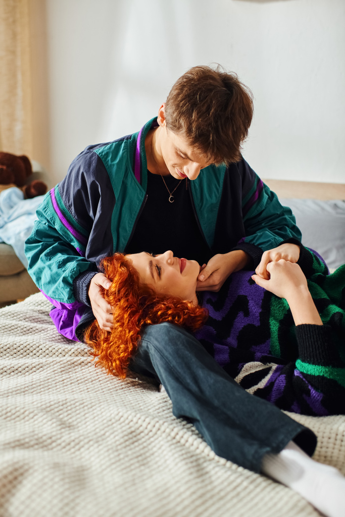 loving good looking young couple in cozy attire hugging warmly while lying on bed at their home - Photo, Image