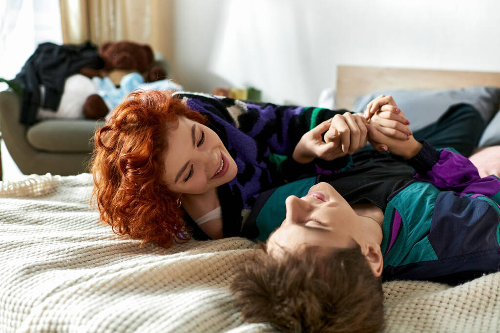 ελκυστικό χαρούμενο ζευγάρι με ζωντανά ρούχα που περνούν υπέροχα μαζί ενώ χαλαρώνουν στο κρεβάτι - Φωτογραφία, εικόνα