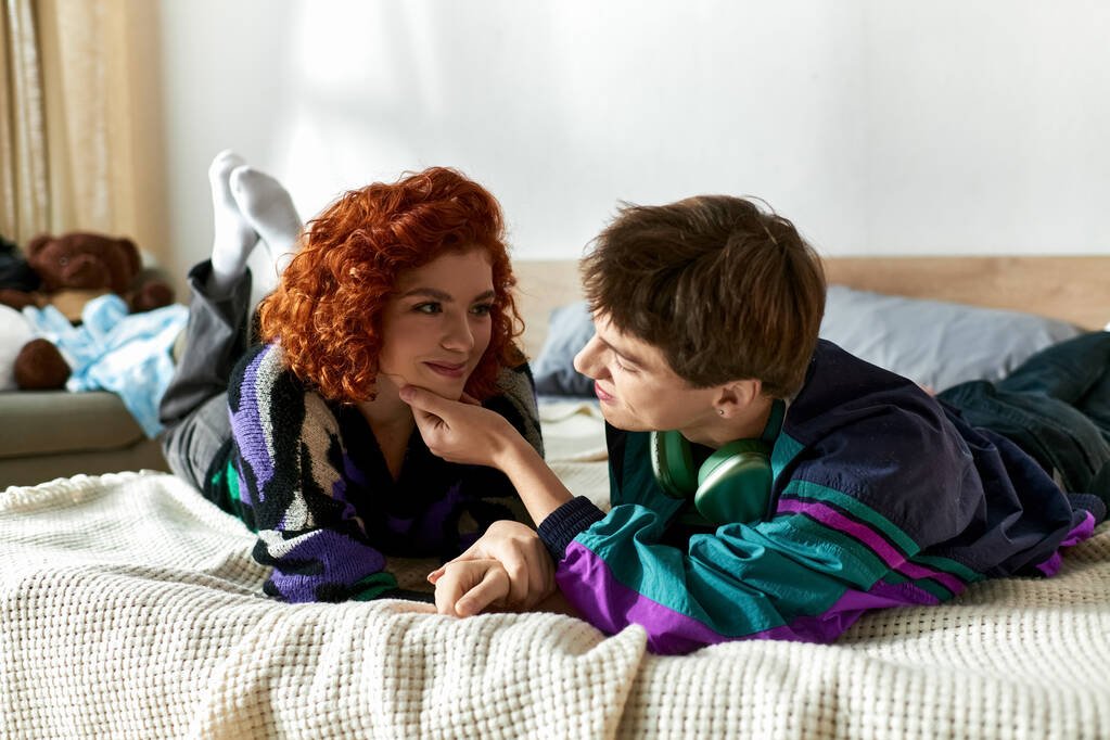 alluring stylish couple in vibrant casual clothes lying in bed together and having great time - Photo, Image