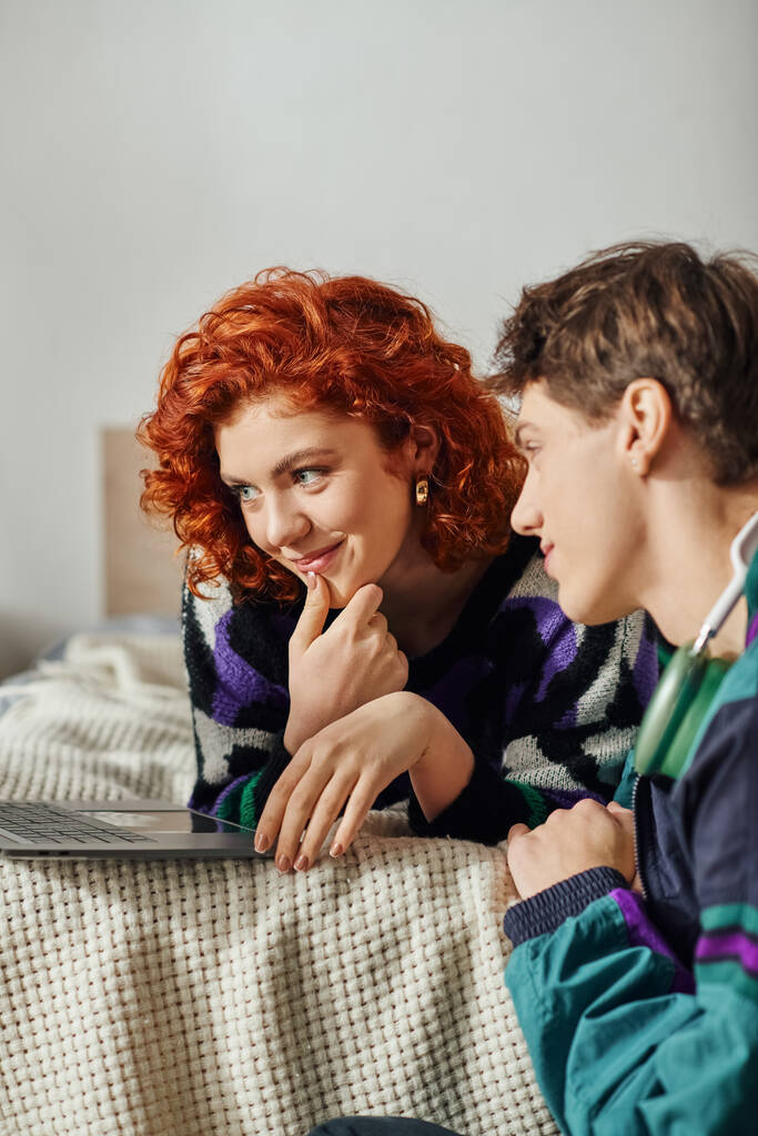 attraktive rothaarige Frau, die neben ihrem hübschen Freund auf dem Bett sitzt und Zeit am Laptop verbringt - Foto, Bild