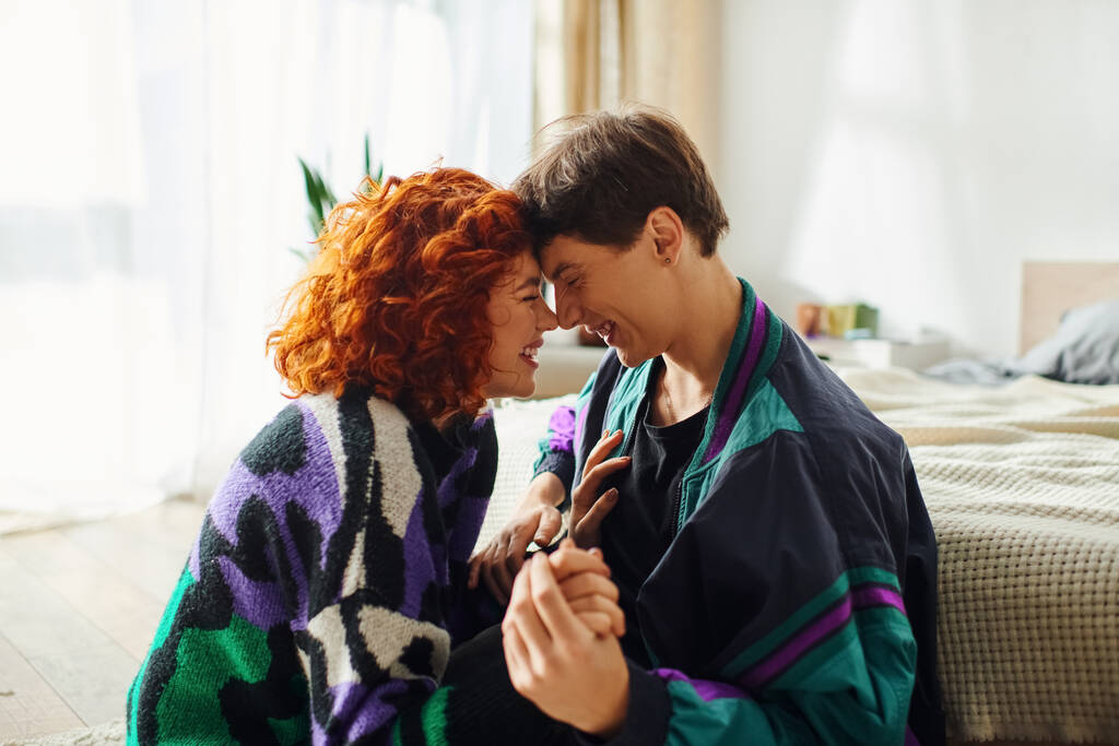 aantrekkelijk liefdevol paar in modieuze kleding kijken naar elkaar terwijl het hebben van plezier thuis - Foto, afbeelding