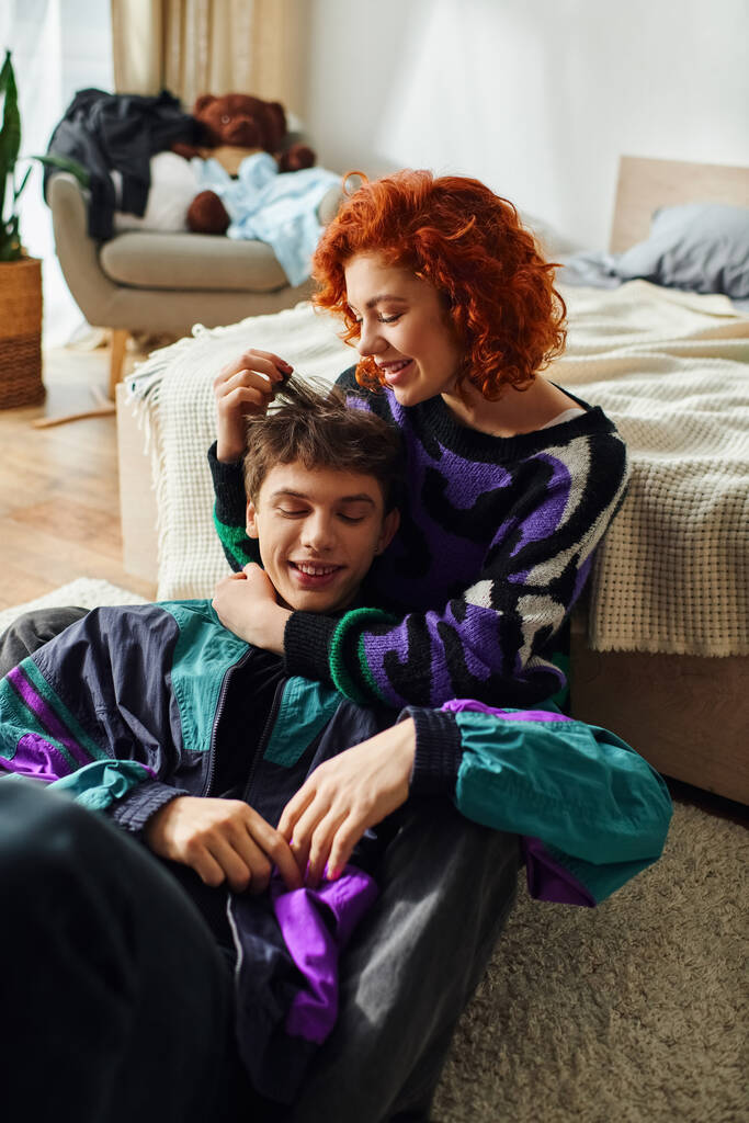 alluring red haired woman in cozy attire spending time with her boyfriend and hugging him lovingly - Photo, Image