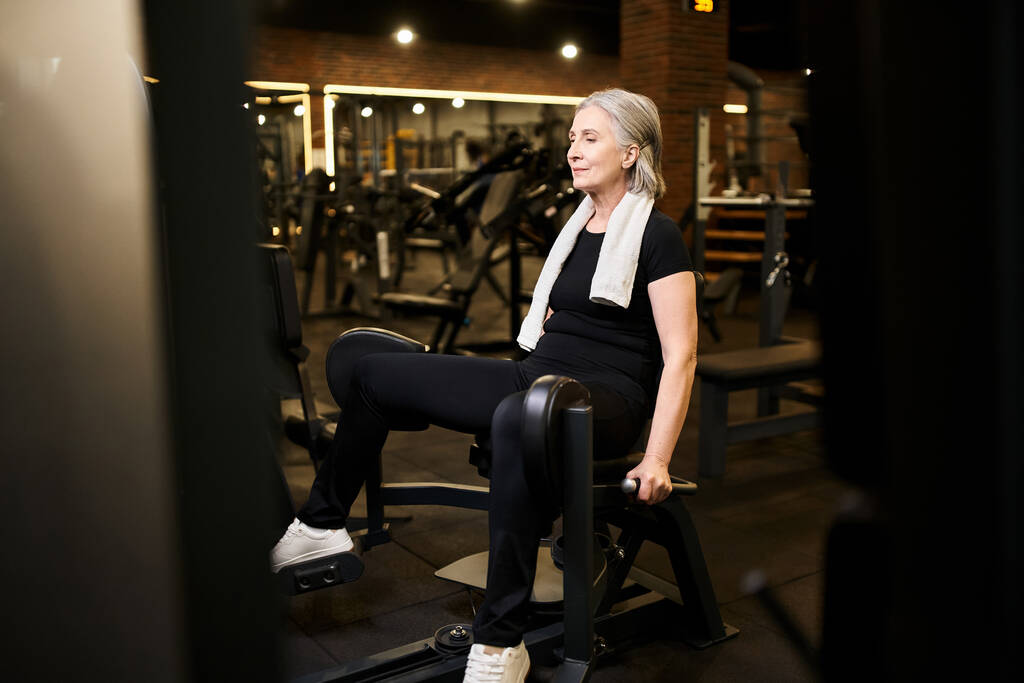 belle sportive sénior joyeux avec cheveux gris et serviette de formation sur la machine à veau tout en salle de gym - Photo, image