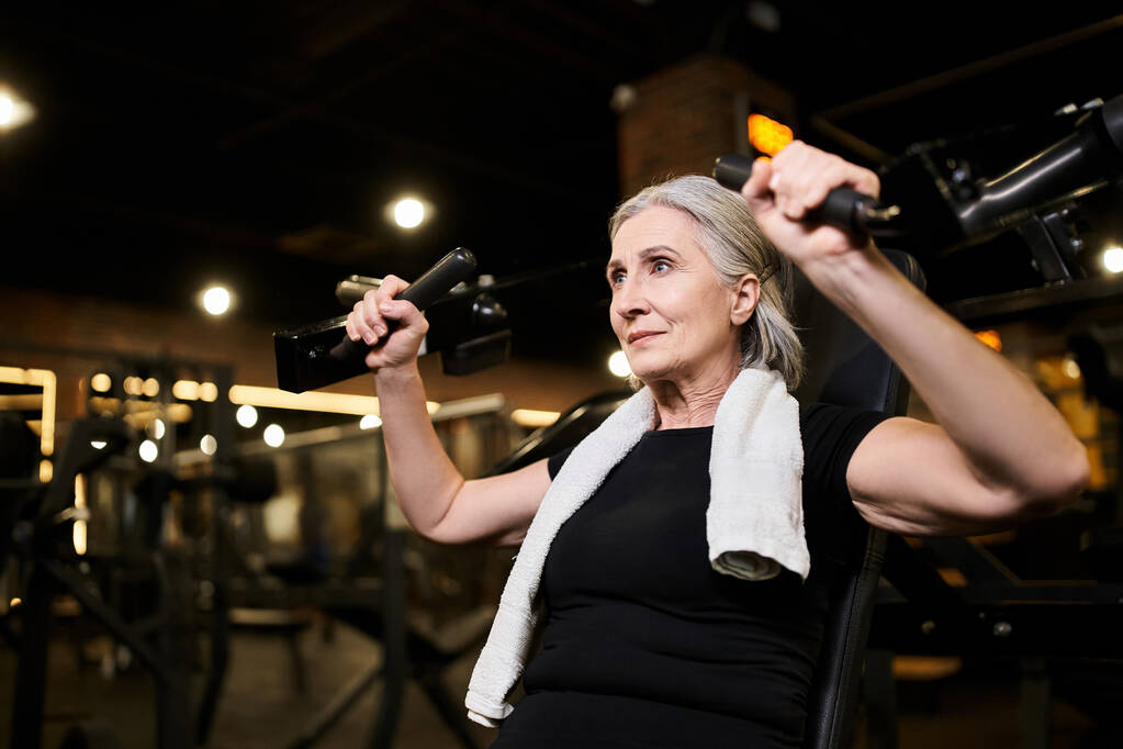 sporty mature beautiful woman in cozy attire exercising actively on chest press machine in gym - Photo, Image